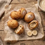 Beignets à la banane dorés et croustillants saupoudrés de sucre glace, disposés sur du papier sulfurisé vu de dessus