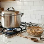 Cocotte-minute en inox sur gazinière avec pois chiches secs dans un bol en verre sur plan de travail en marbre blanc