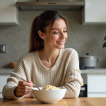 Femme en sweater oatmeal dégustant un bol de porridge dans une cuisine lumineuse